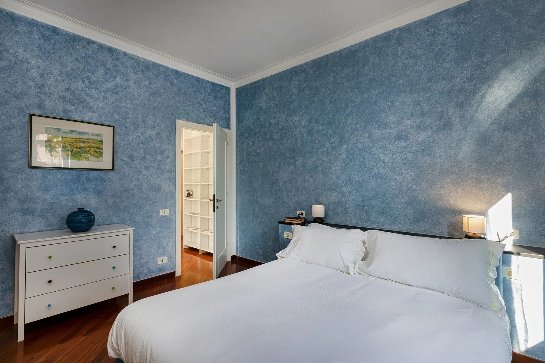 Un dormitorio con una cama grande, paredes azules y una cómoda blanca.