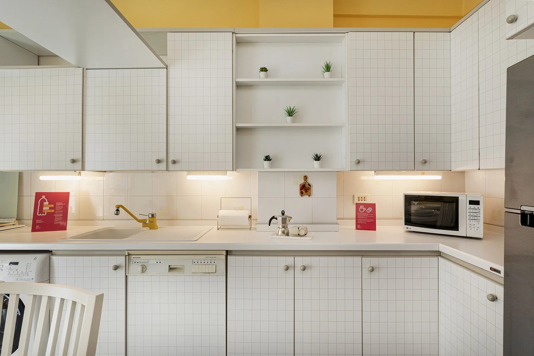 Una cocina luminosa con armarios blancos, un fregadero y un microondas.