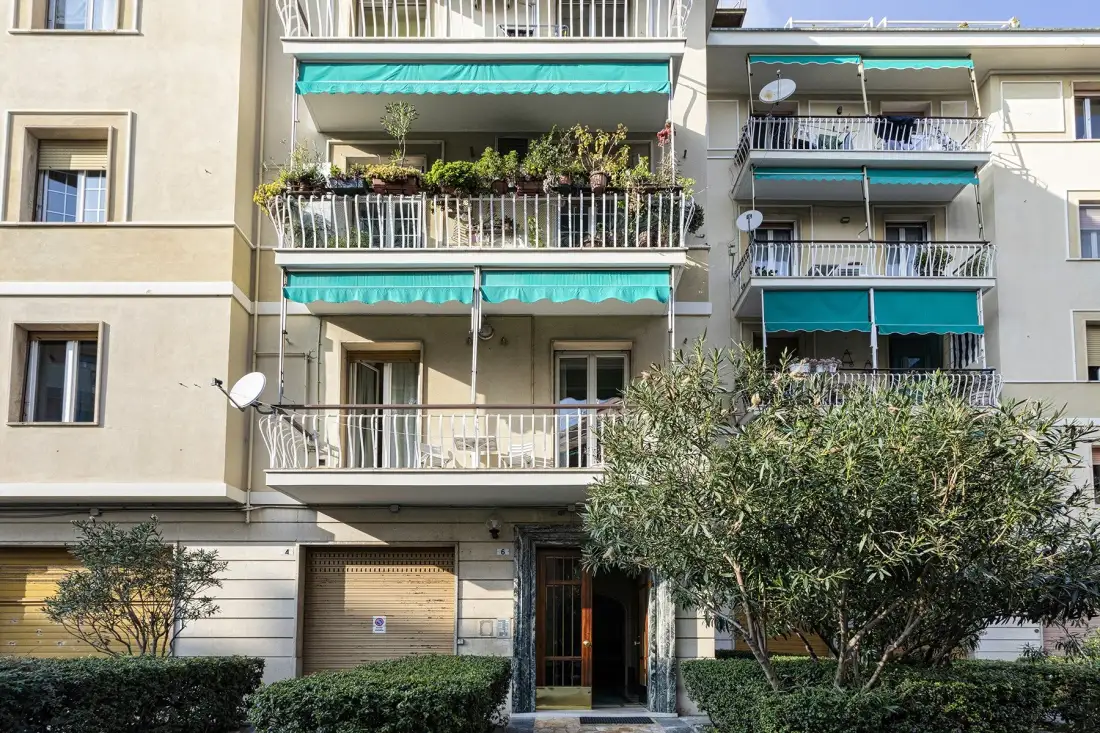 Edificio de apartamentos con balcones, toldos verdes y árboles.