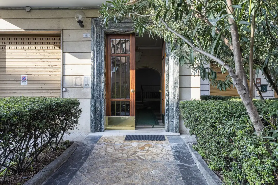 La entrada de un edificio da a un sendero de piedra bordeado de arbustos y árboles.