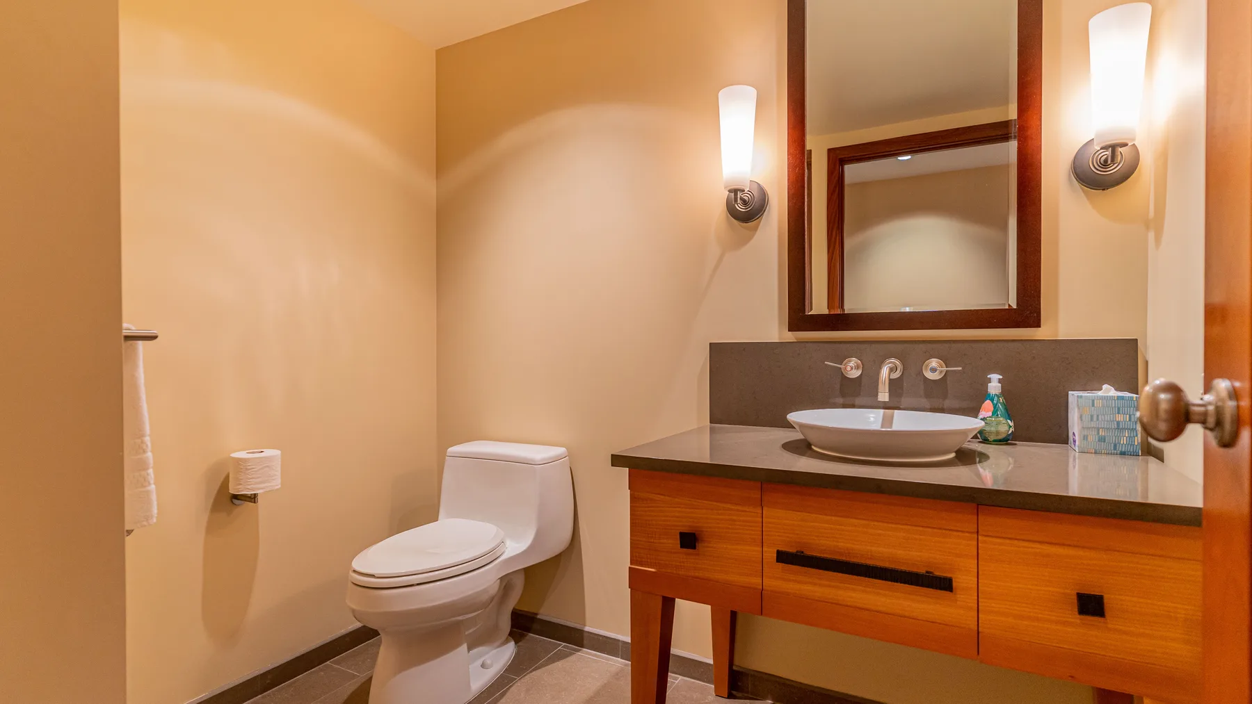 Un baño con un inodoro y un tocador de madera bajo un espejo.