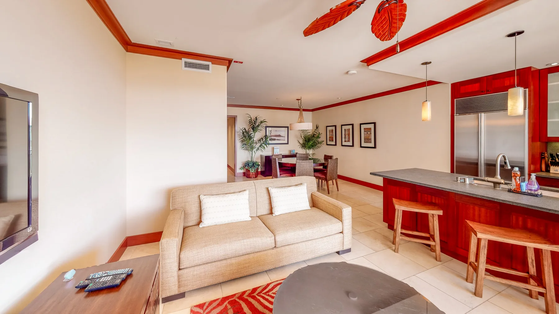Una sala luminosa con un sofá beige y una isla de cocina roja.