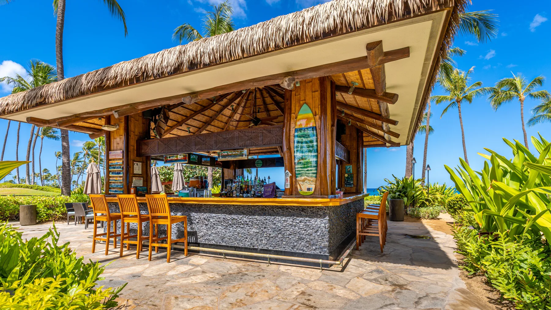 Un bar al aire libre con techo de paja y asientos de madera en un entorno tropical.