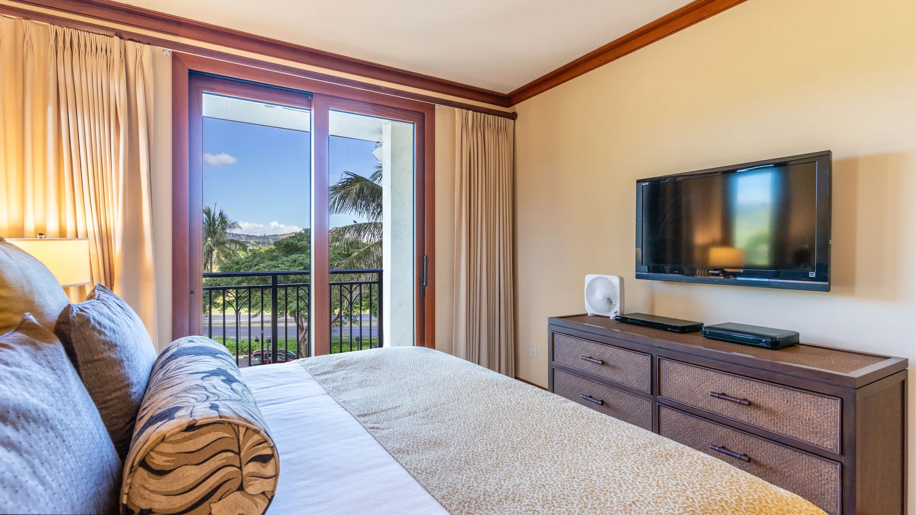 Un dormitorio con cama, televisor y puertas corredizas de vidrio con vistas a la vegetación.