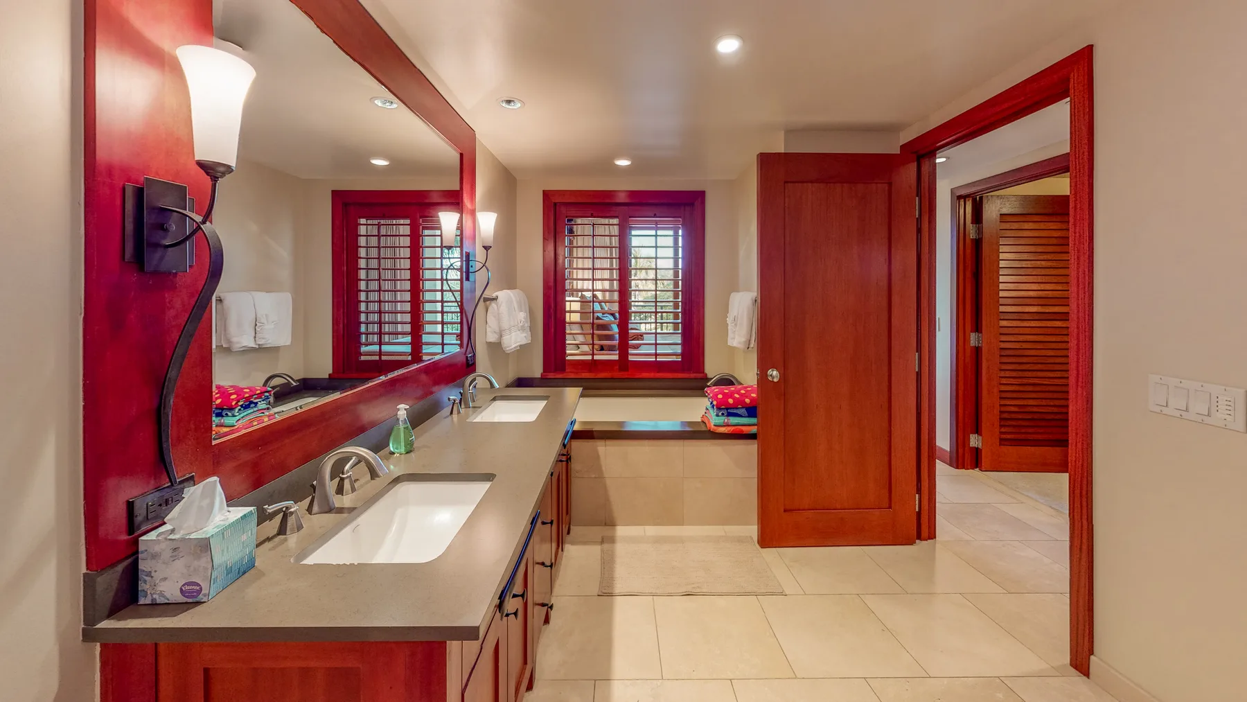 Un tocador de baño con lavabo y espejo da a ventanas con marcos rojos.