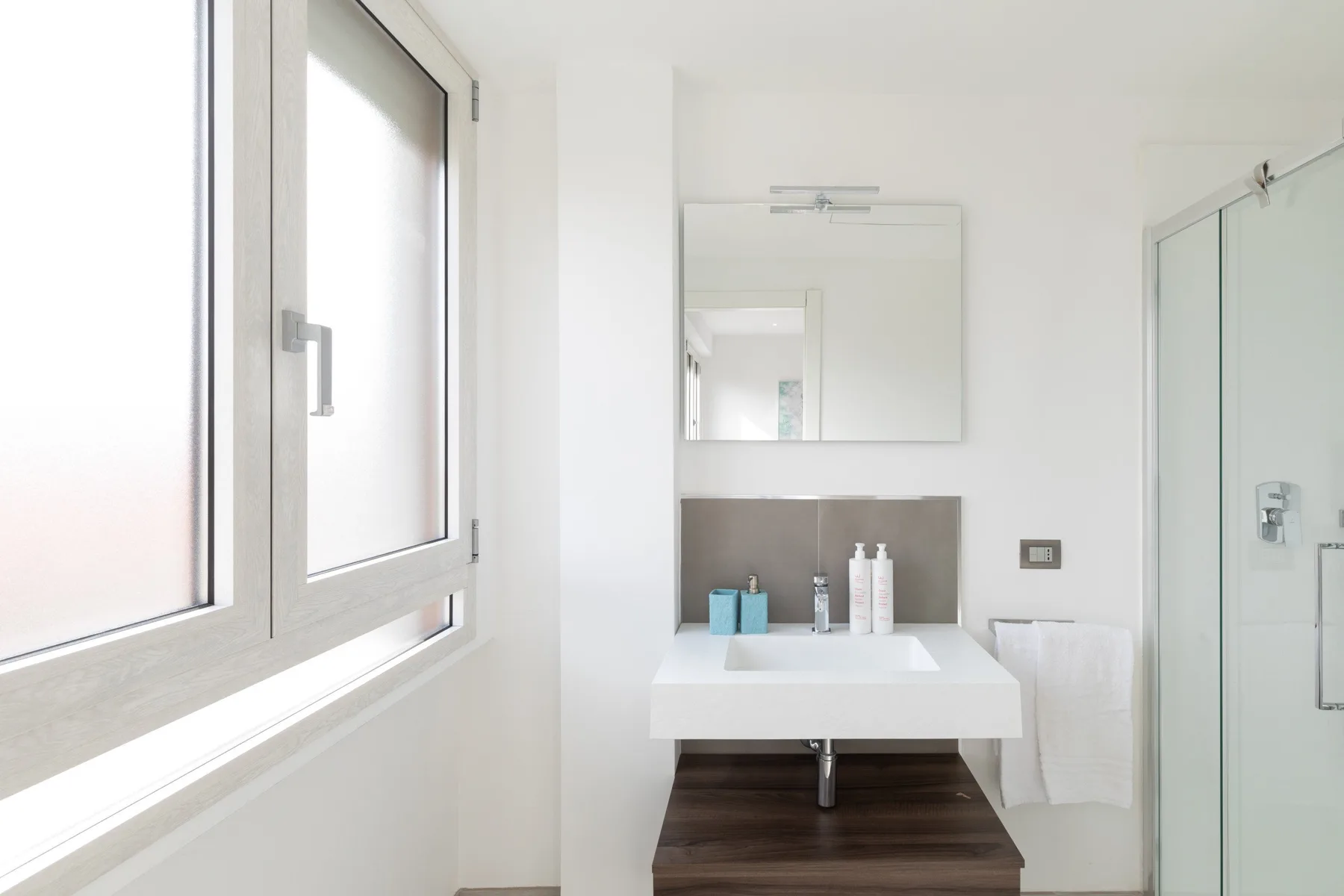 Un baño luminoso con un lavabo bajo un espejo de pared y una ducha de cristal.