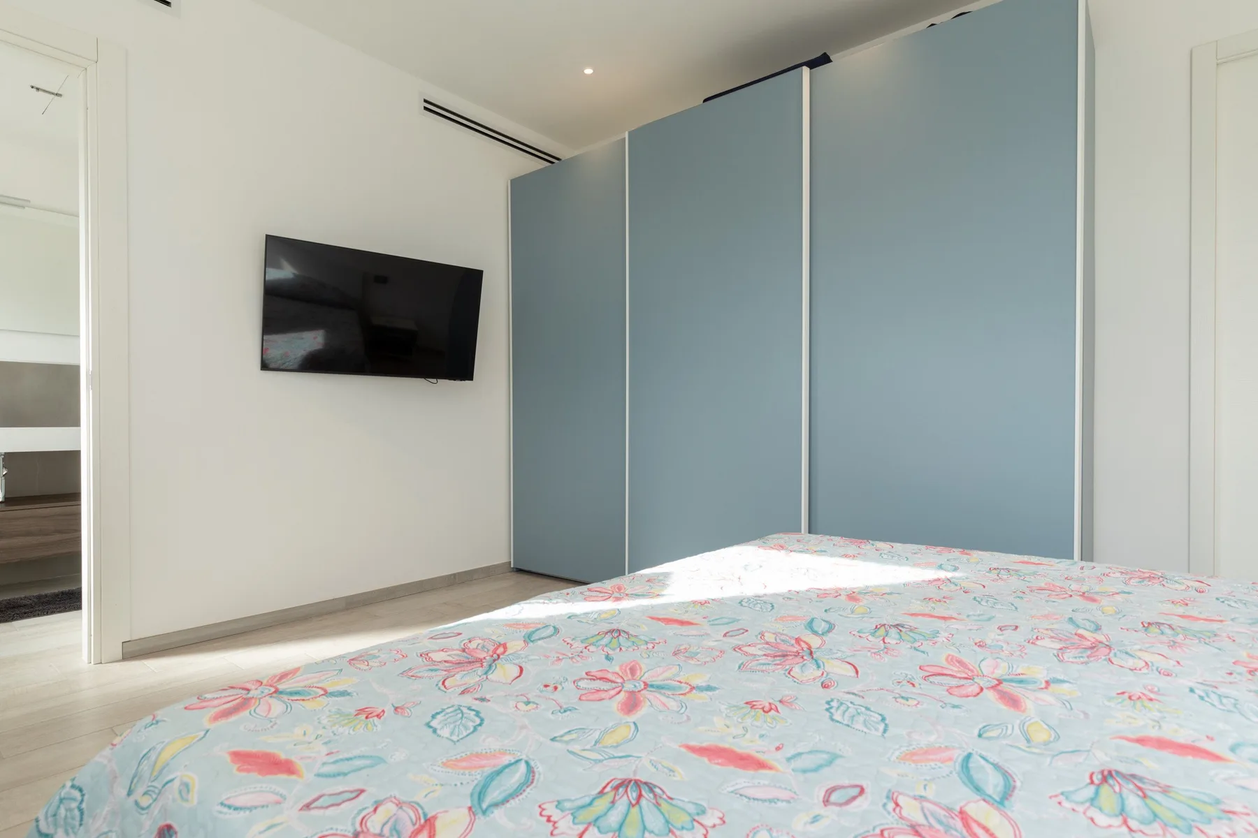 Un dormitorio con una colcha floral colorida, un televisor en la pared y armarios azules.