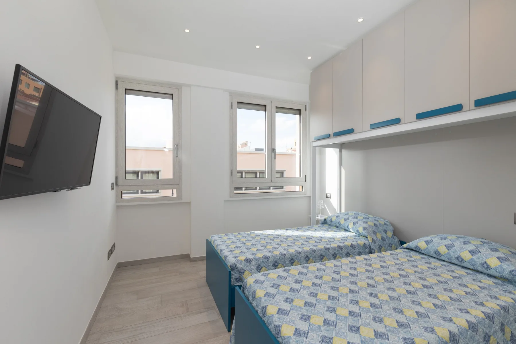 Un dormitorio luminoso con dos camas, armarios empotrados y un televisor en la pared.