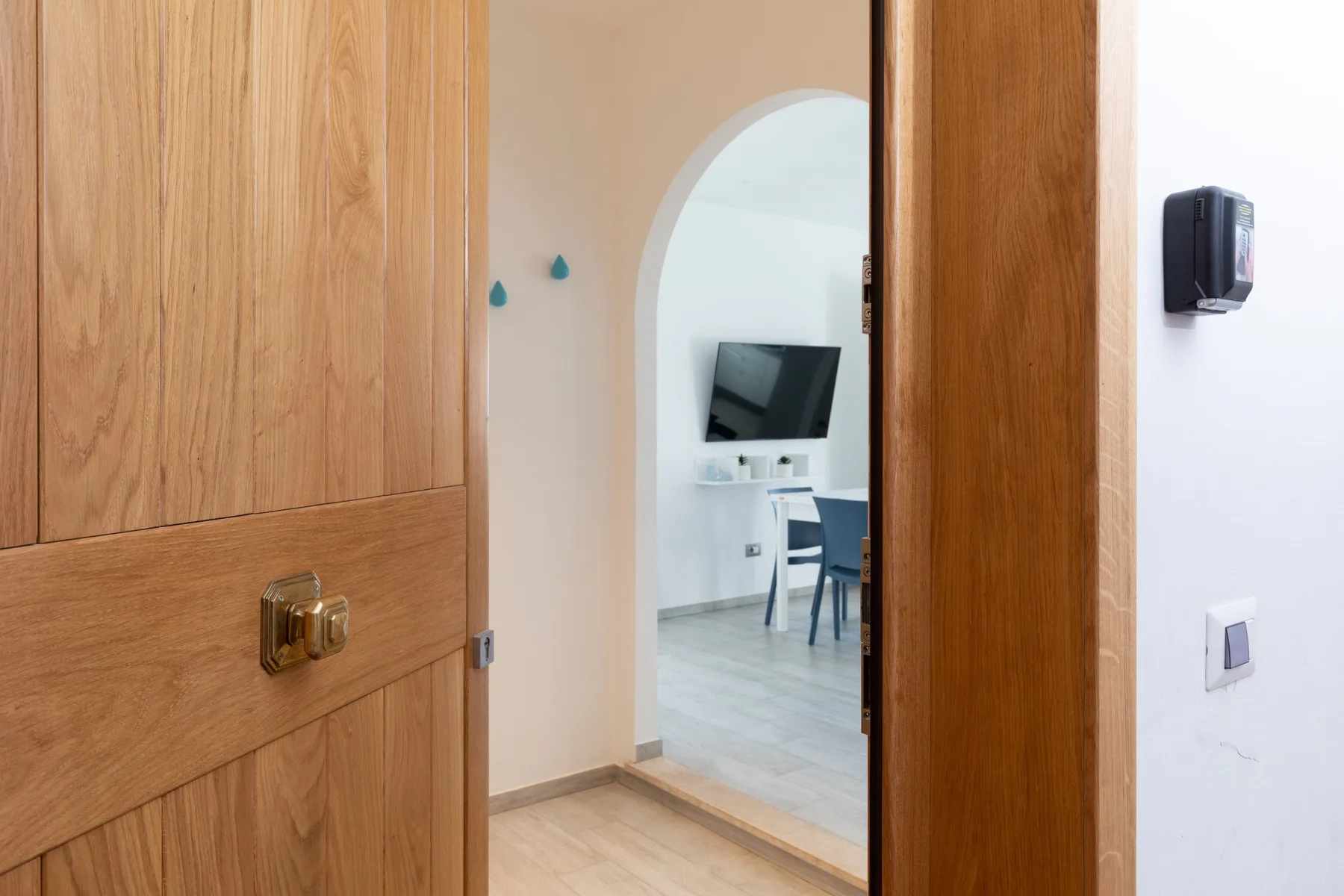Una puerta de madera abierta da a una habitación luminosa con escritorio y sillas.