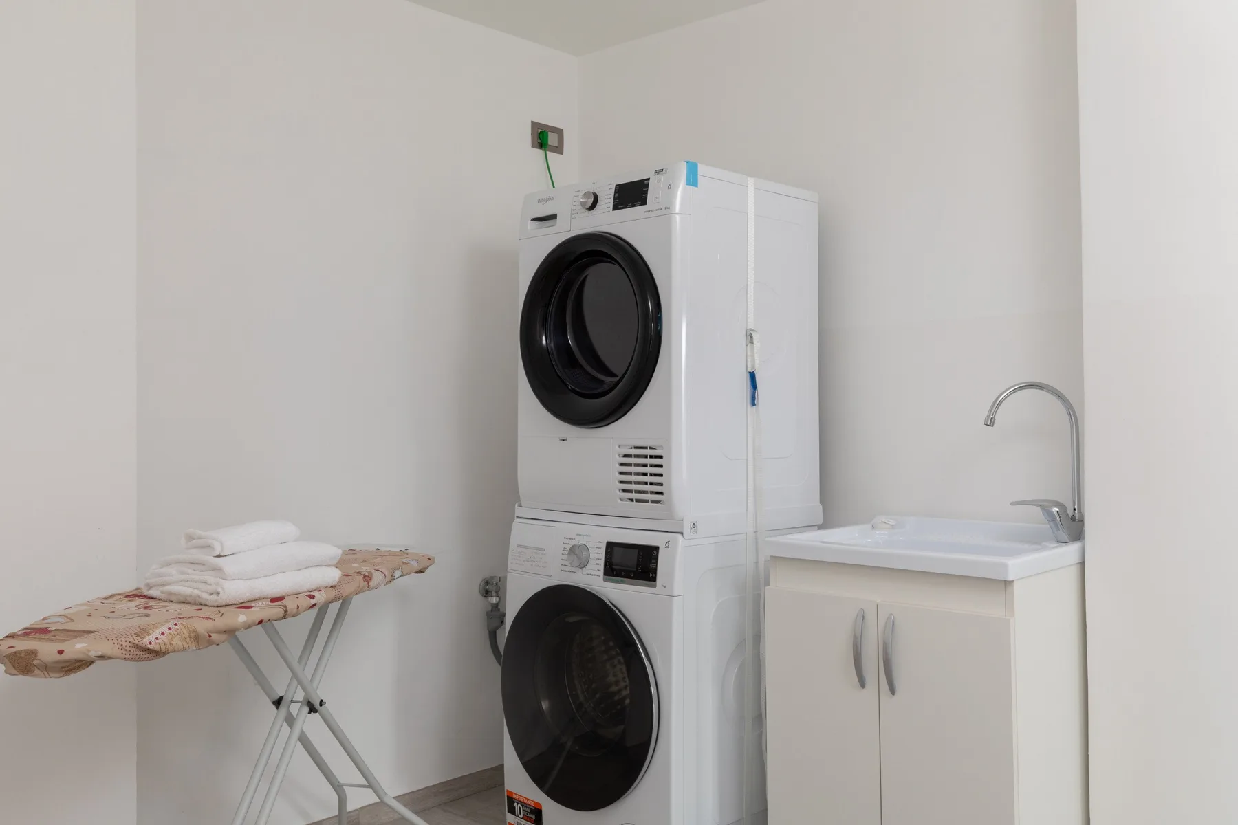 Una zona de lavandería con lavadoras apiladas junto a un mueble con fregadero.