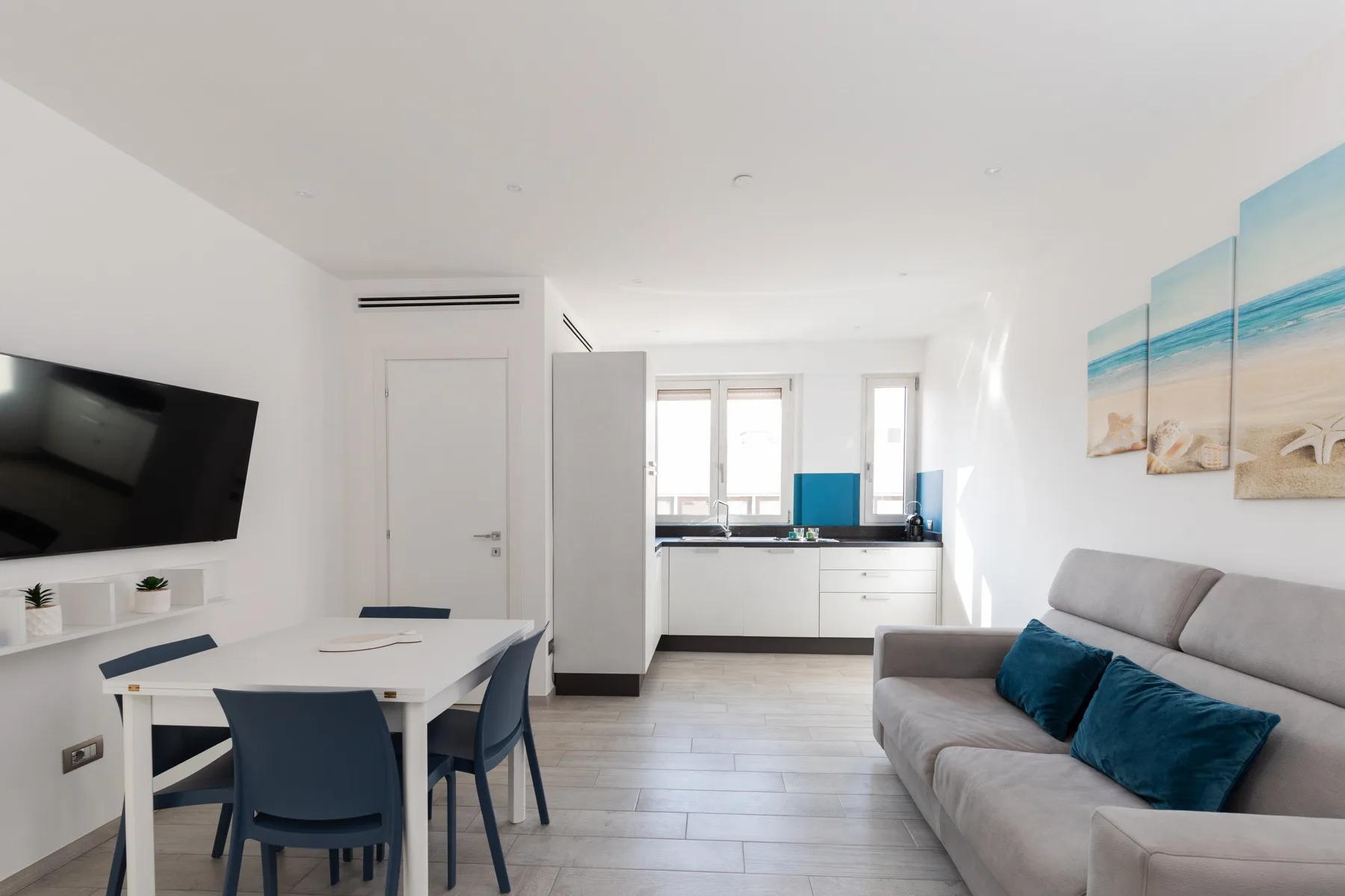 Una luminosa sala-comedor con sofá gris, mesa y cocina.