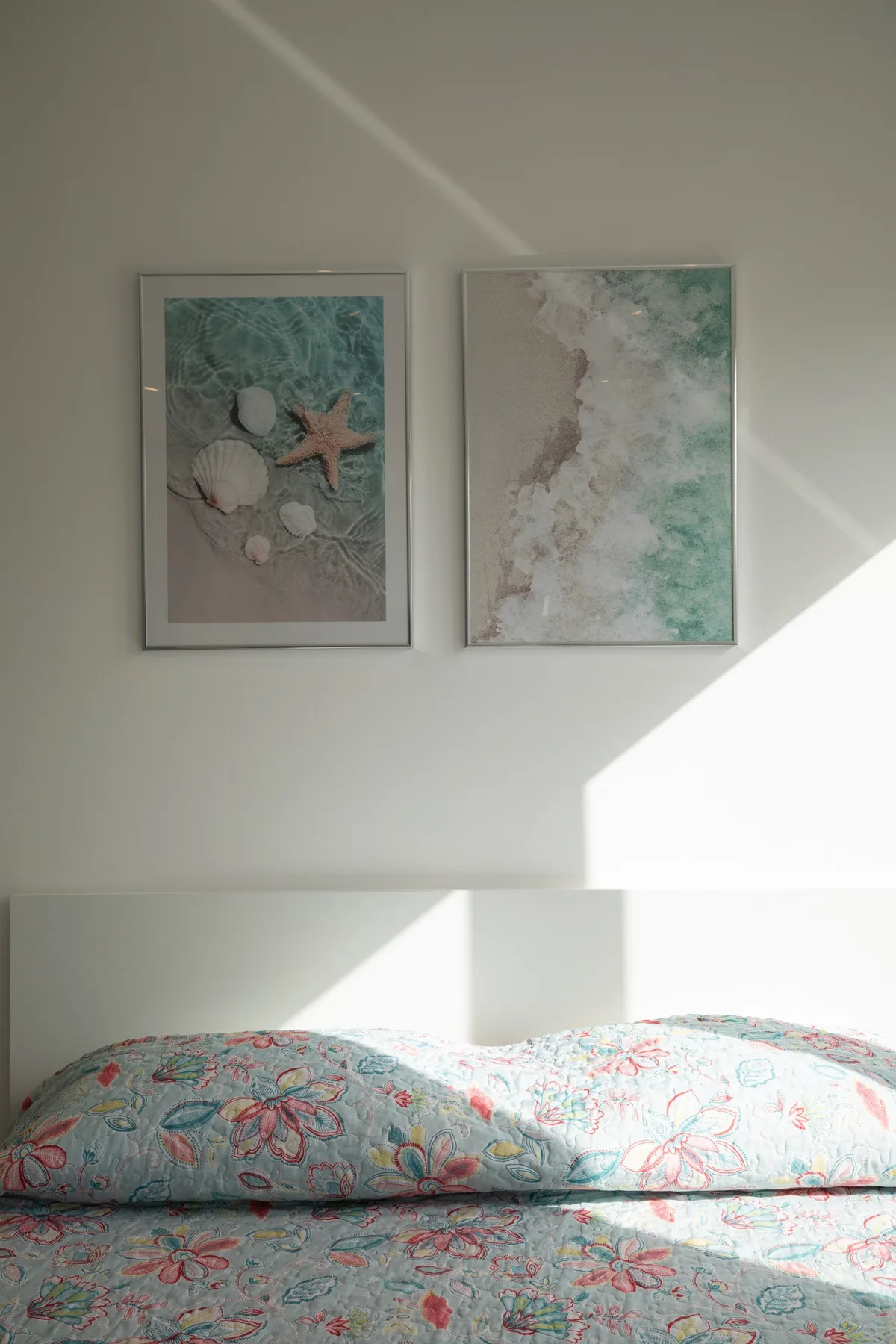 Una cama con una colcha floral está bajo dos láminas costeras enmarcadas.