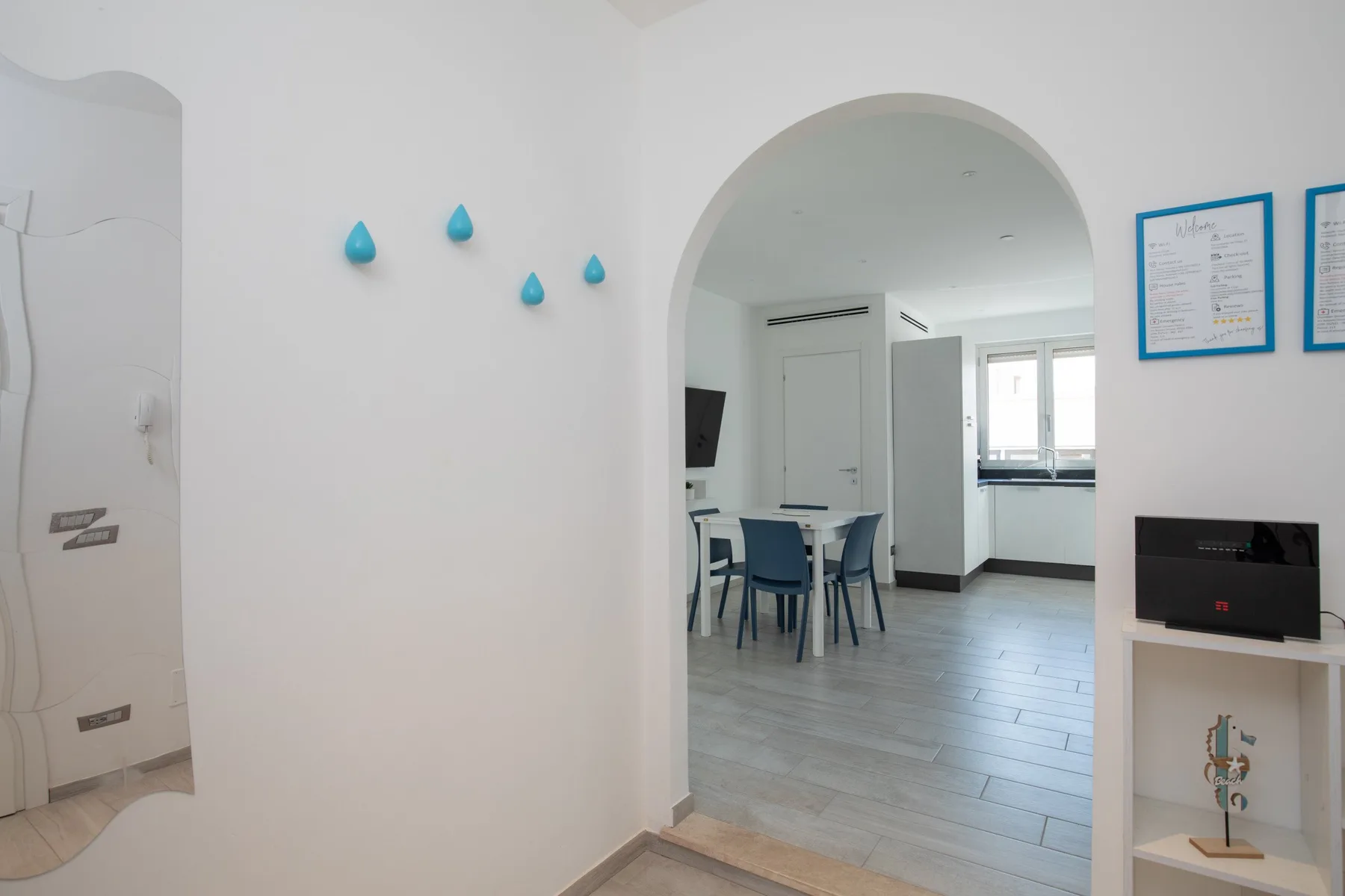 A través de un arco se ve un comedor luminoso con una mesa y asientos azules.