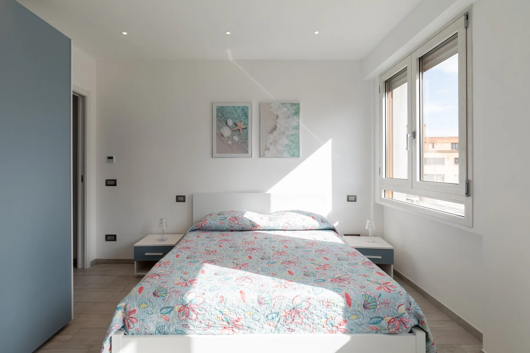 Un dormitorio luminoso con una cama cubierta con una colcha estampada de flores junto a una ventana grande.