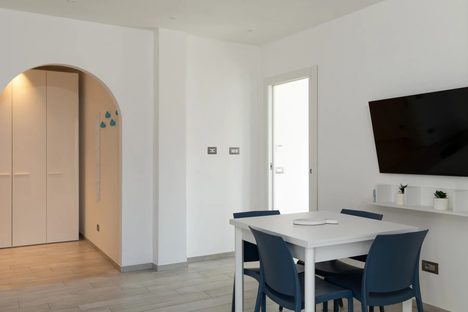 Un comedor luminoso con una mesa blanca y asientos azules junto a un vano en arco.