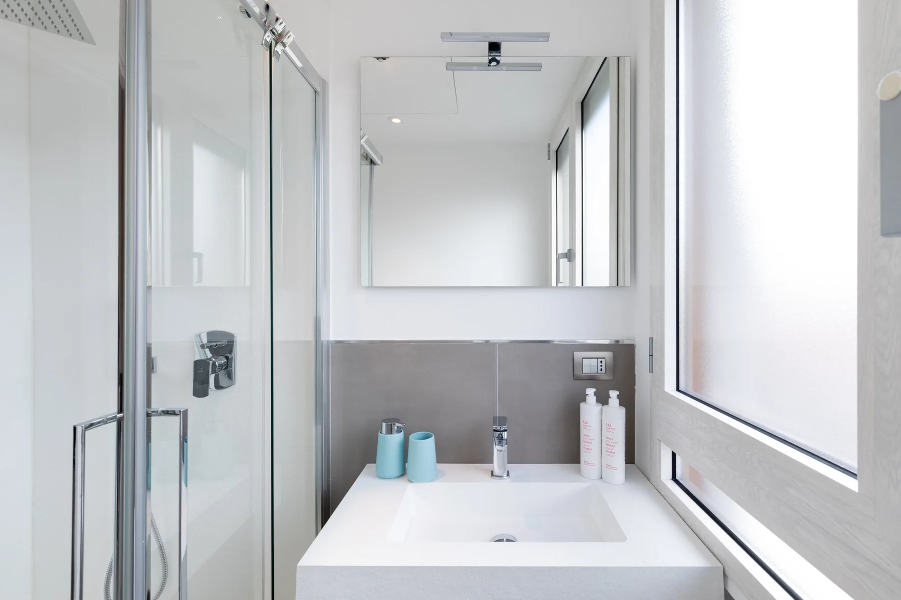 Un baño luminoso con un lavabo amplio, espejo y ducha de vidrio.