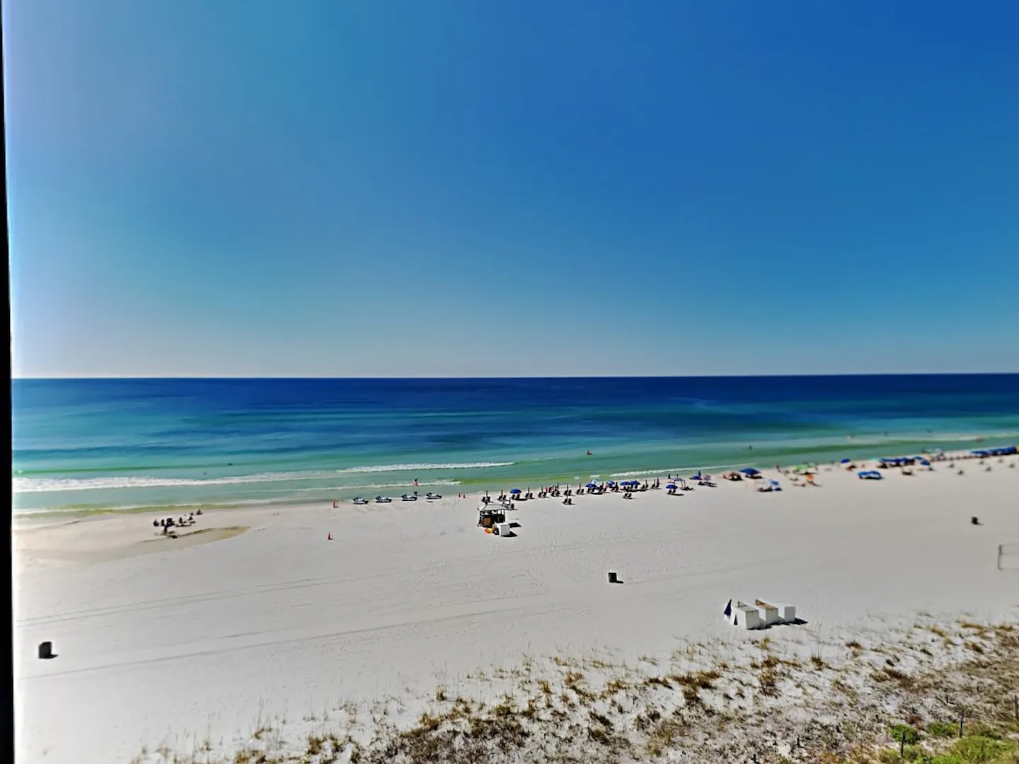 A broad sandy beach meets turquoise water beneath a clear blue sky.