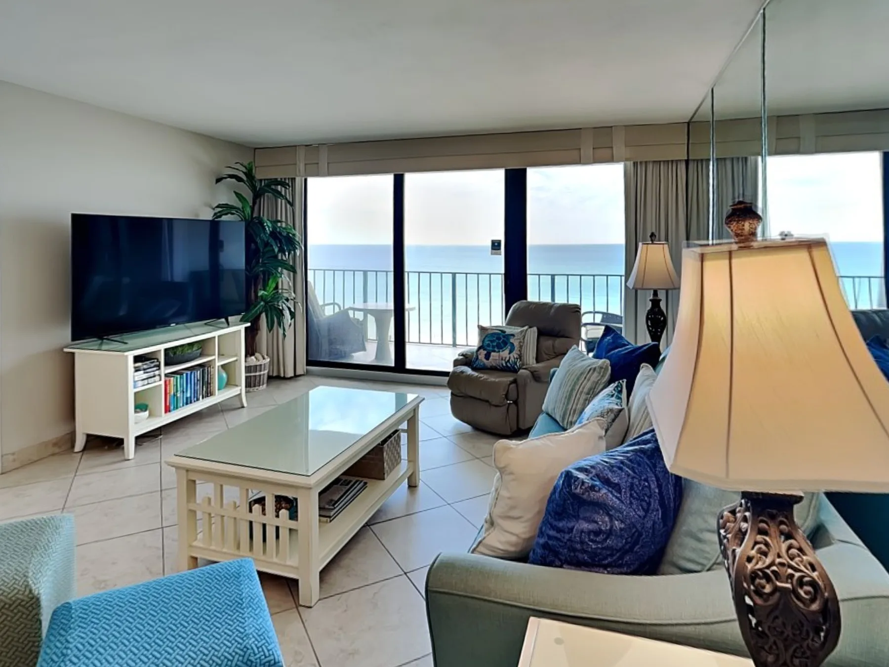 A living room with seating and a television beside large windows overlooking the water.