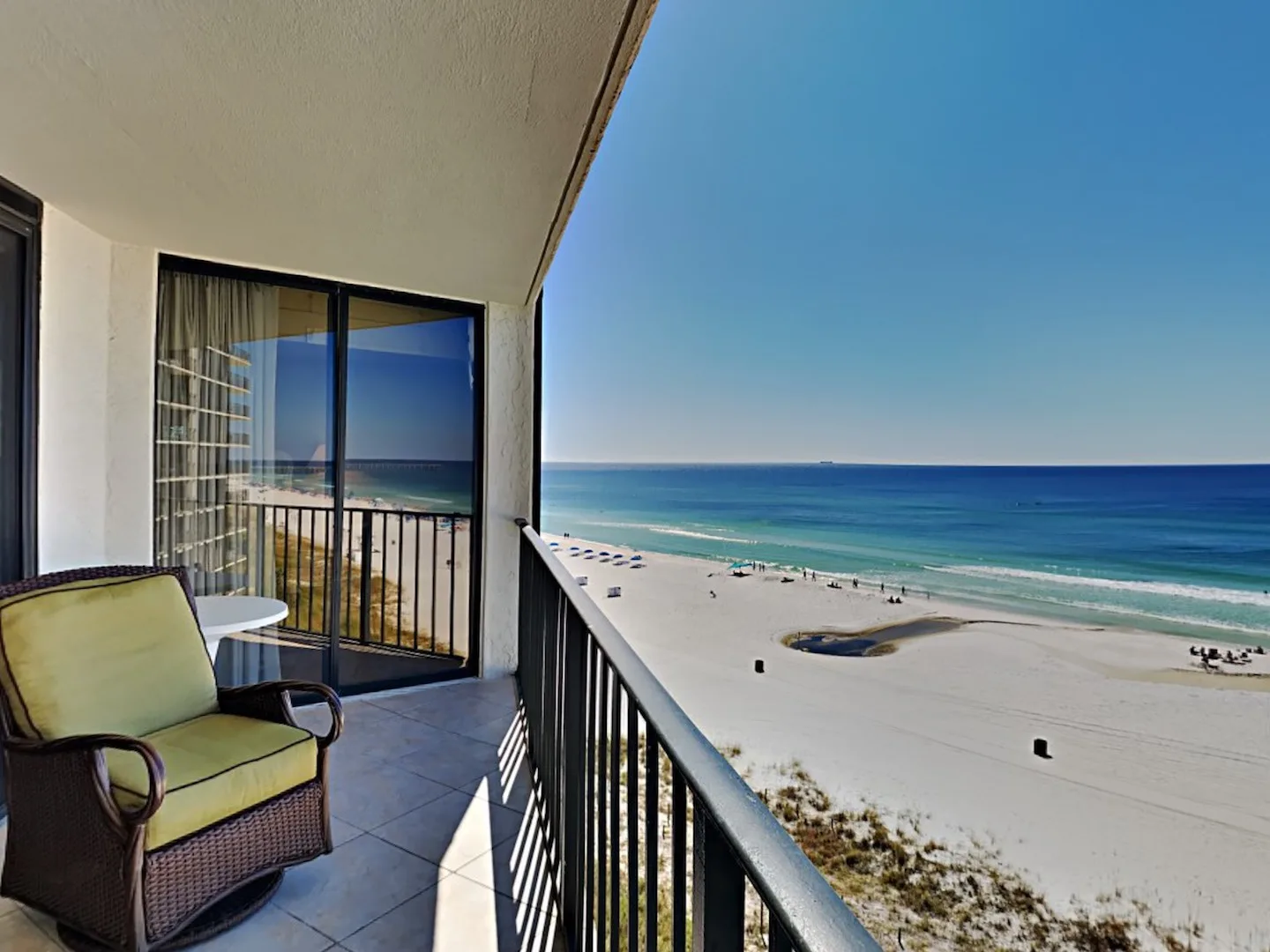 A balcony overlooks a sandy beach and ocean, with seating beside the railing.
