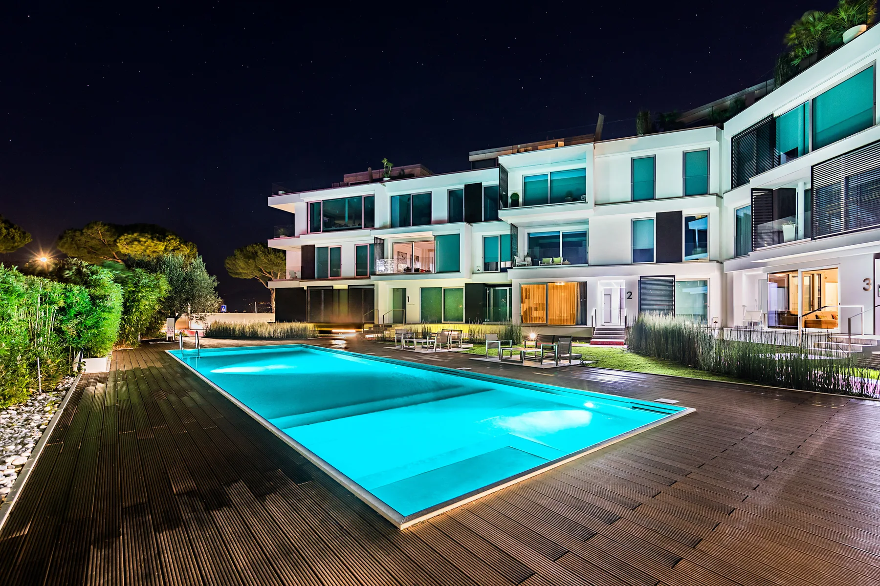 Una piscina y una terraza de madera están frente a un edificio moderno de noche.