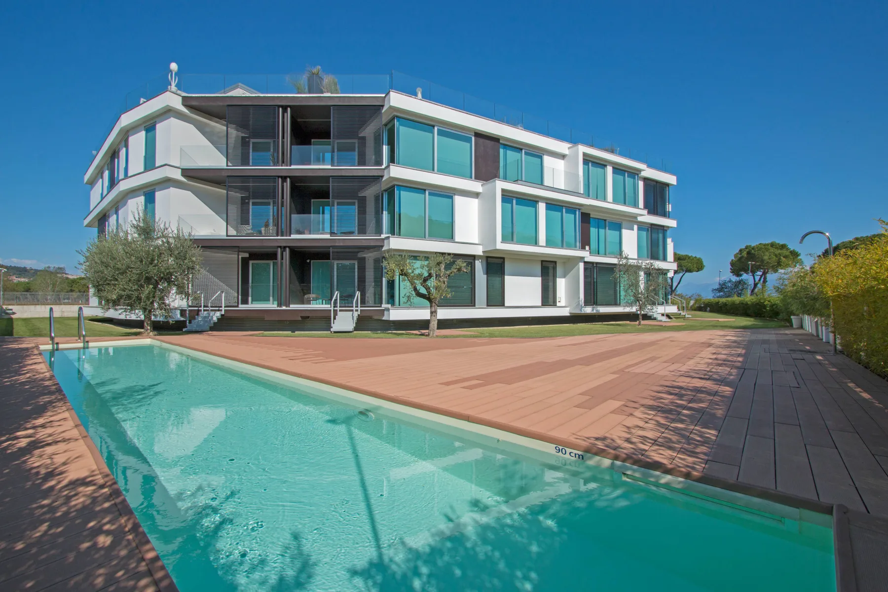 Un edificio moderno da a una piscina y una amplia terraza pavimentada.
