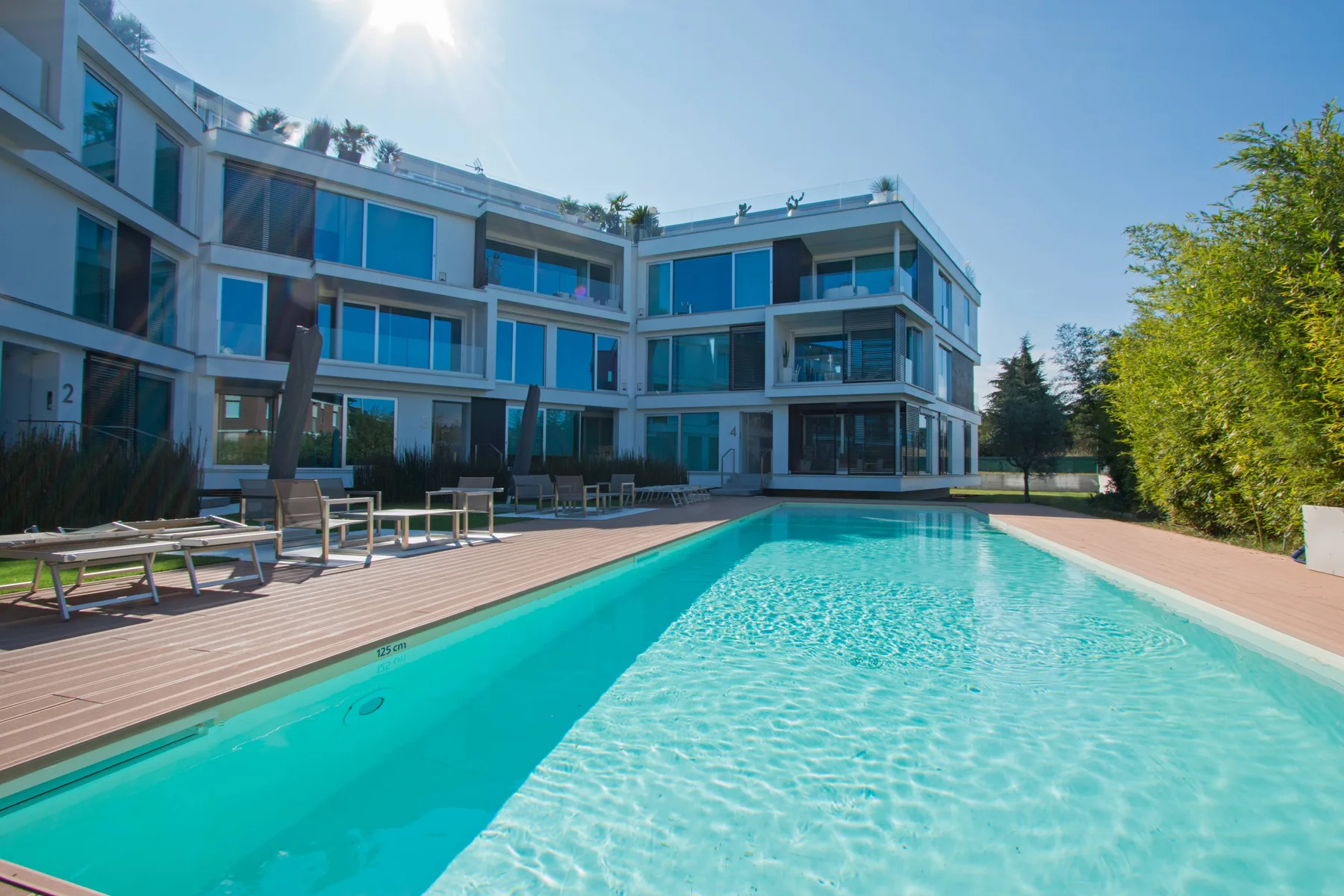 Una piscina está junto a un edificio moderno de varios pisos y una terraza.