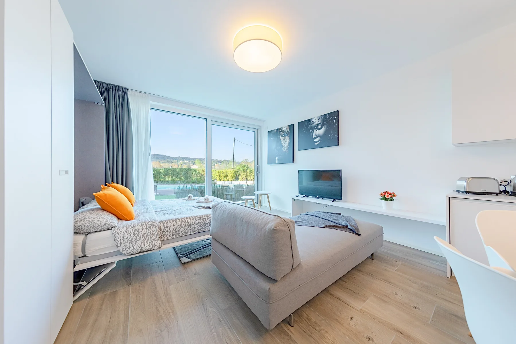 Una sala luminosa con un sofá, una cama de día y grandes ventanas.