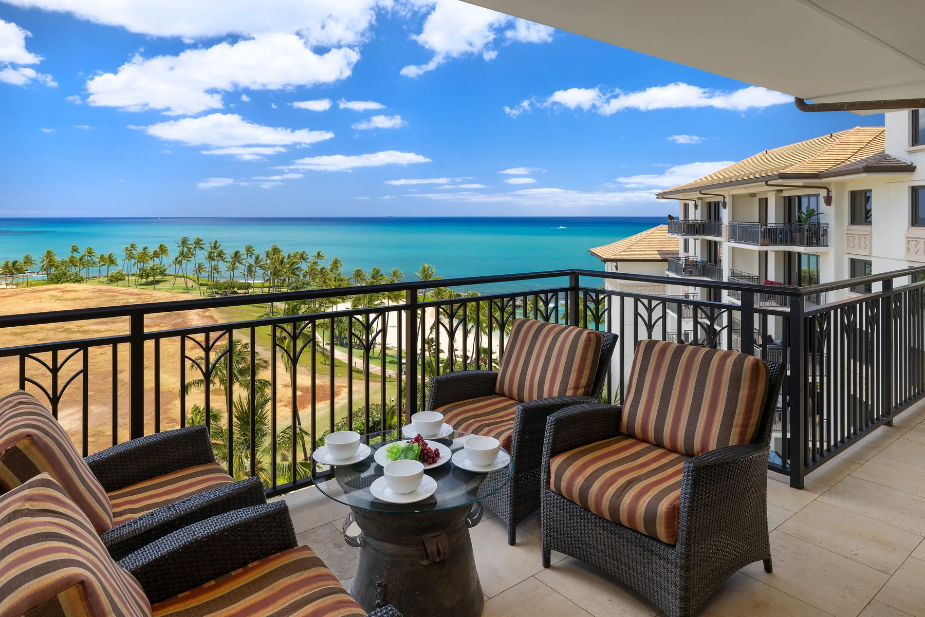 A balcony seating area overlooks palm trees and the ocean.