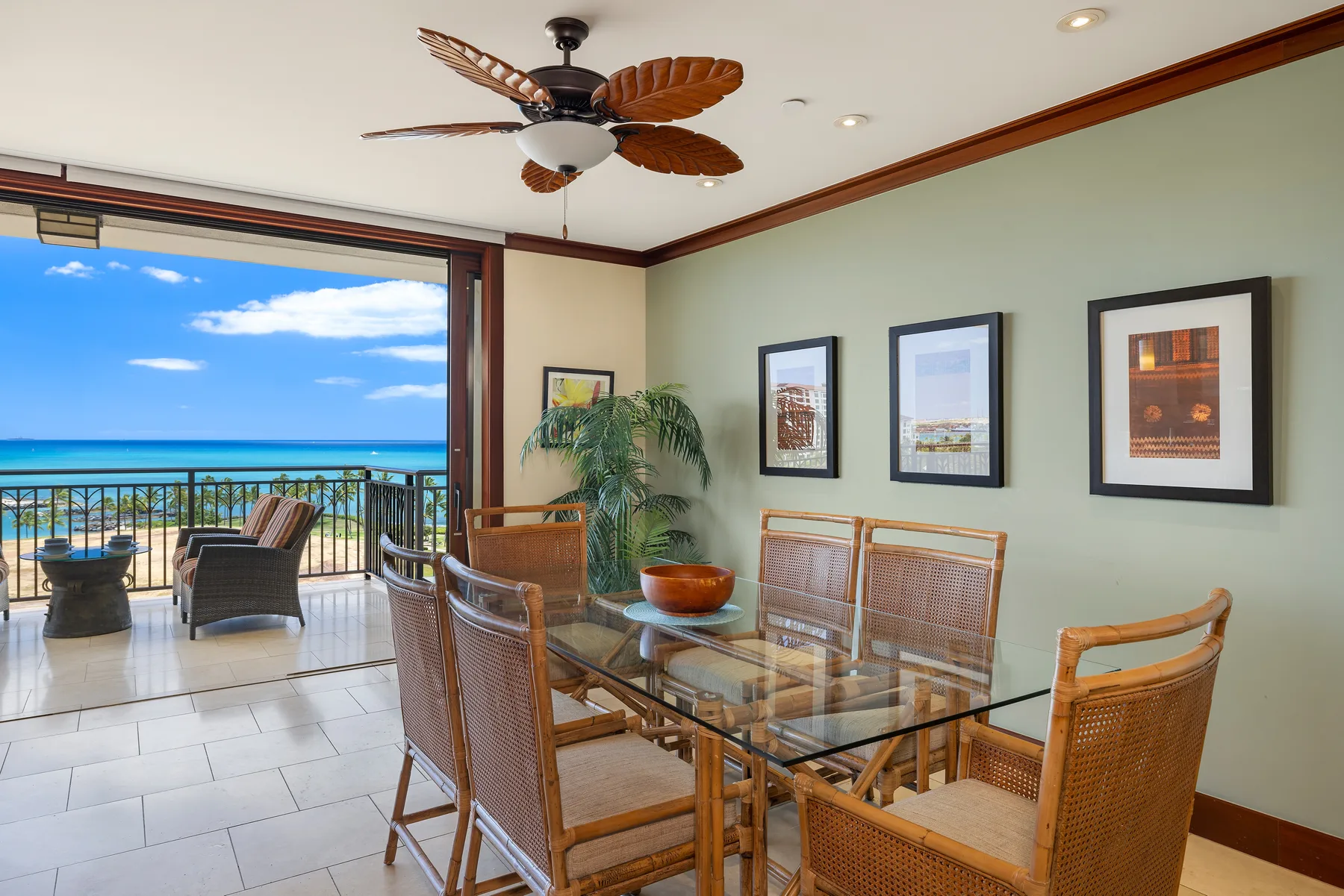 A dining area with wicker seating and a glass table opens onto a balcony overlooking the ocean.