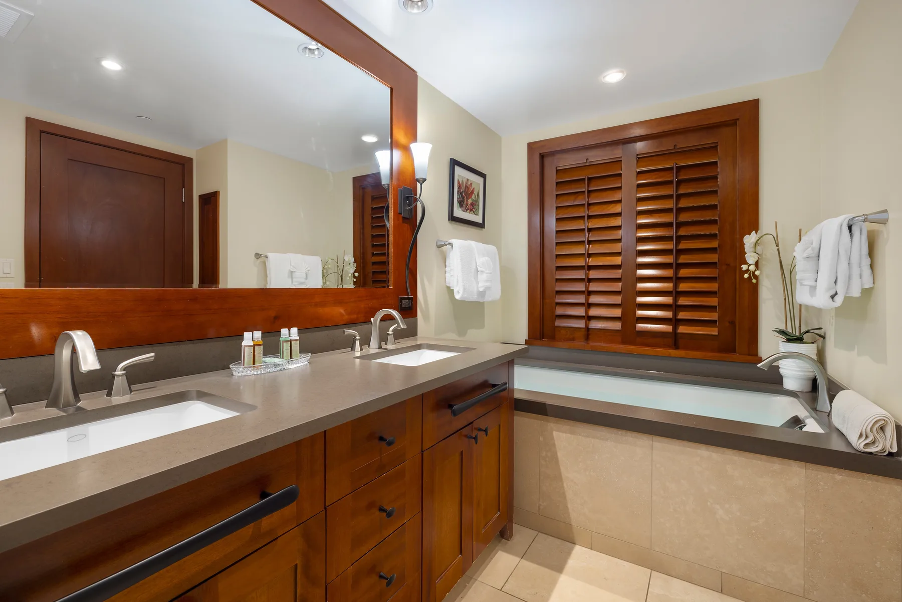A bathroom vanity with a wide mirror faces a bathtub beneath a window.
