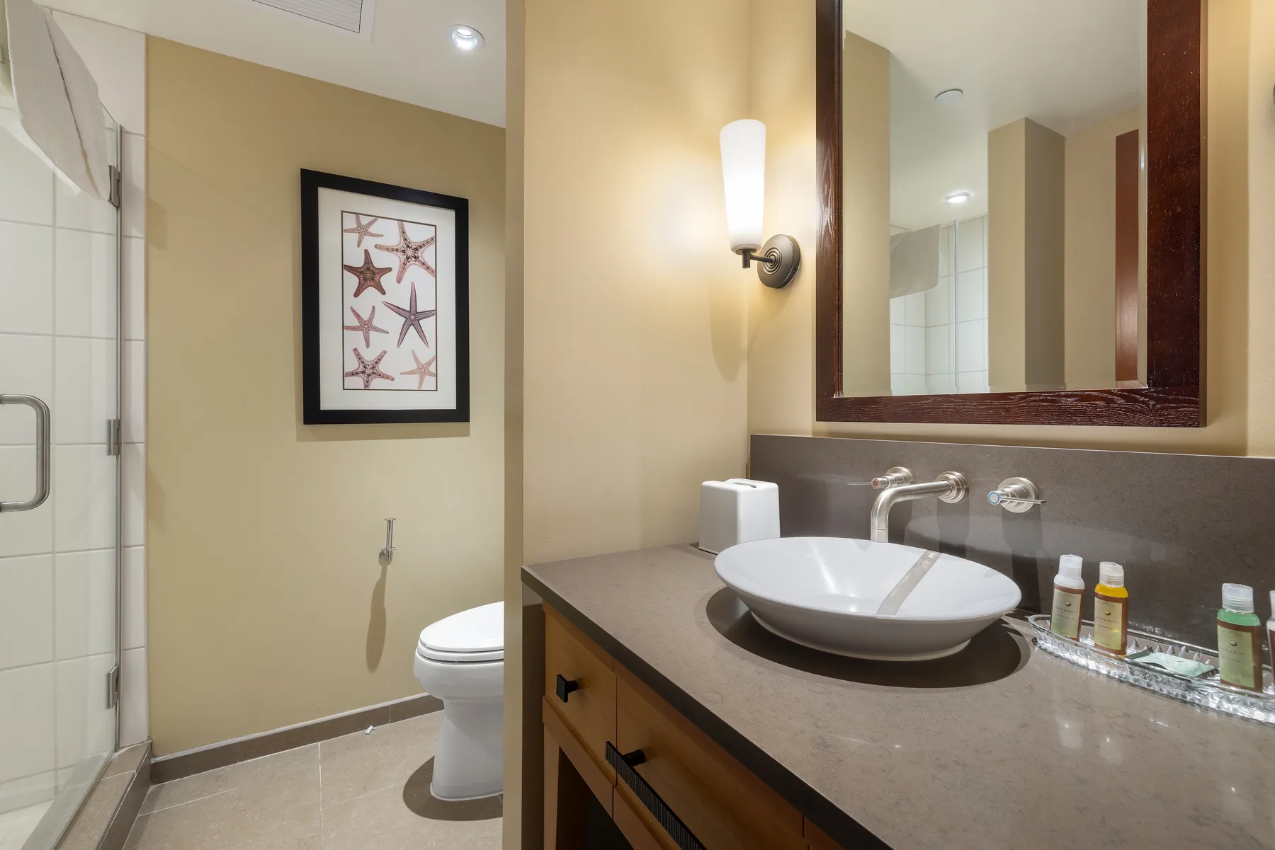 A bathroom vanity with a vessel sink and a toilet beside the shower.