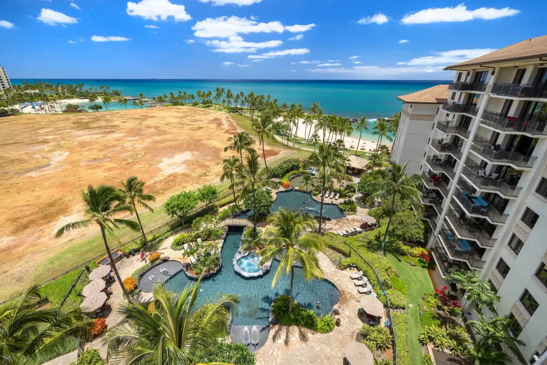 Aerial view of a coastal resort with a pool, palm trees, and the ocean.