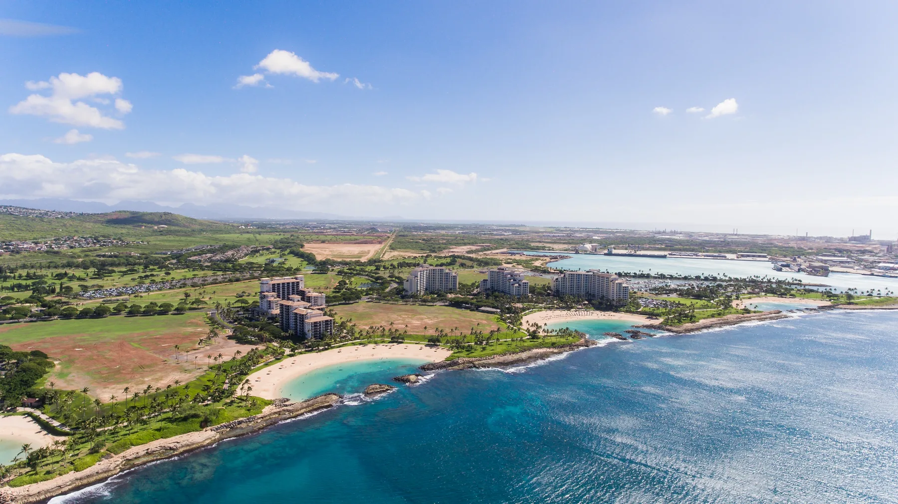 Aerial coastal view of turquoise water, a curved beach, and green land.