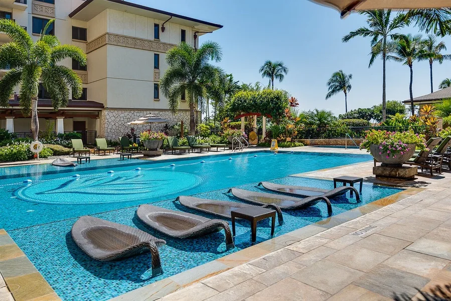 An outdoor swimming pool with submerged loungers beside a landscaped hotel building.
