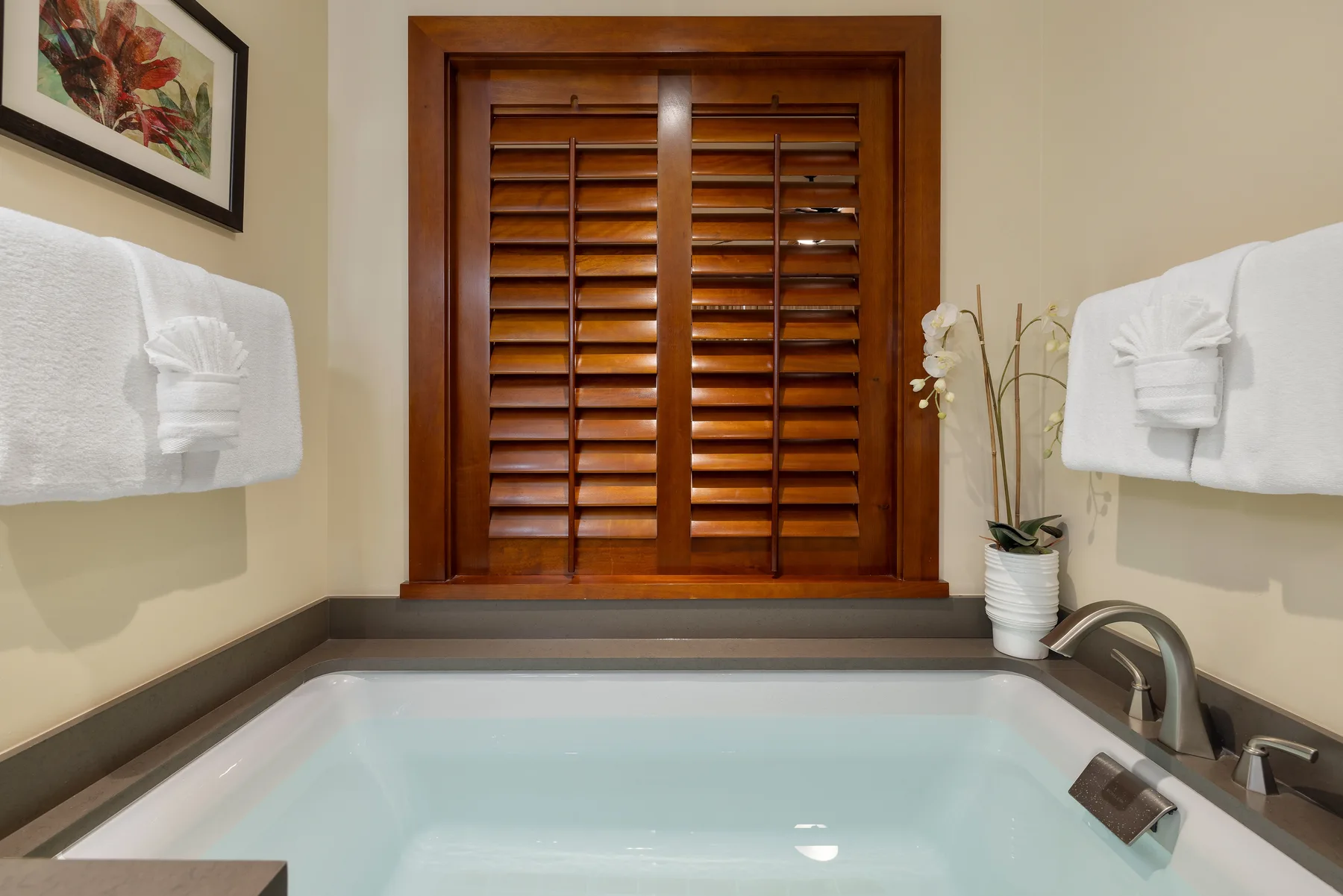 A bathroom soaking tub sits beneath a wooden shuttered window.