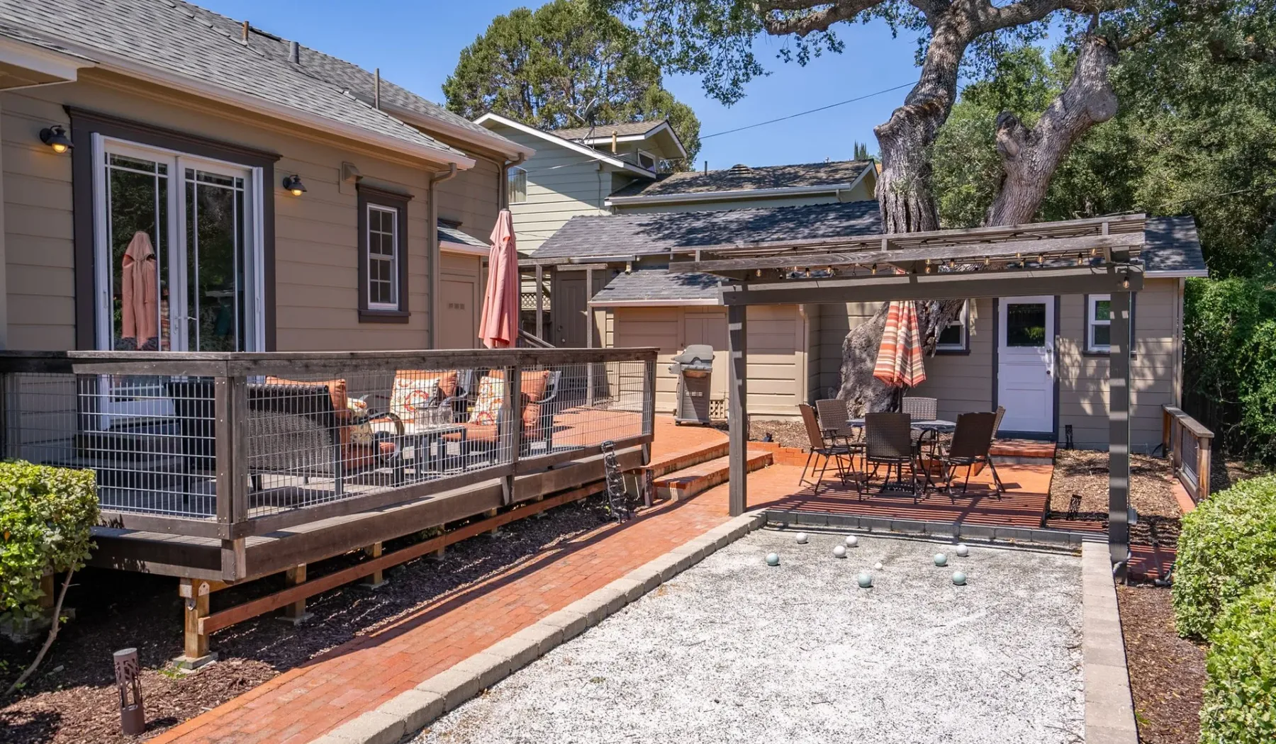 Un patio al aire libre con una zona de grava para juegos y una mesa bajo una pérgola de madera.