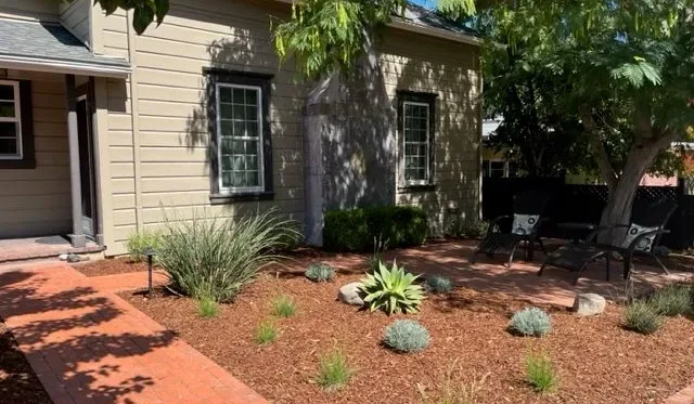 Un jardín junto a una casa beige, con asientos de patio bajo un árbol.