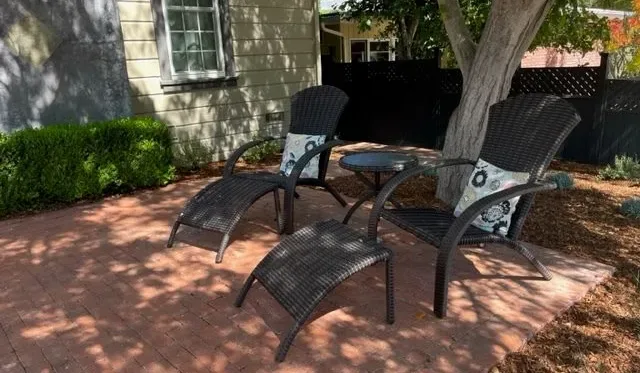 Un patio al aire libre con asientos reclinables bajo un árbol.
