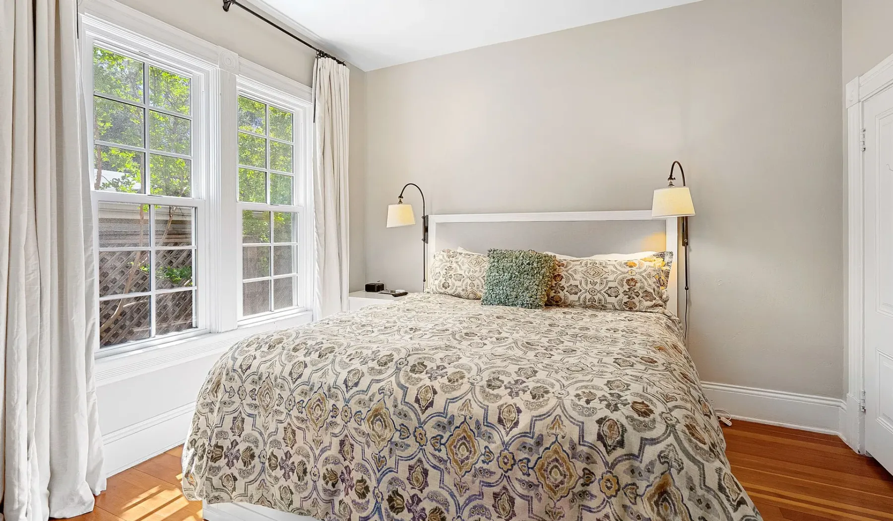 Un dormitorio con una cama estampada junto a dos ventanas.