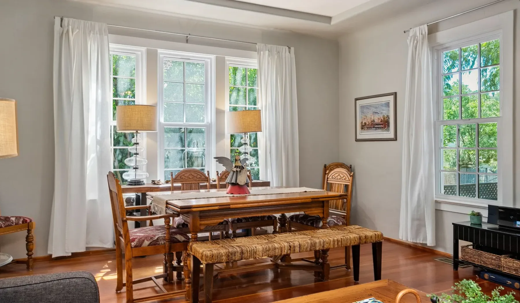 Un comedor con una mesa y sillas de madera junto a grandes ventanas con cortinas.