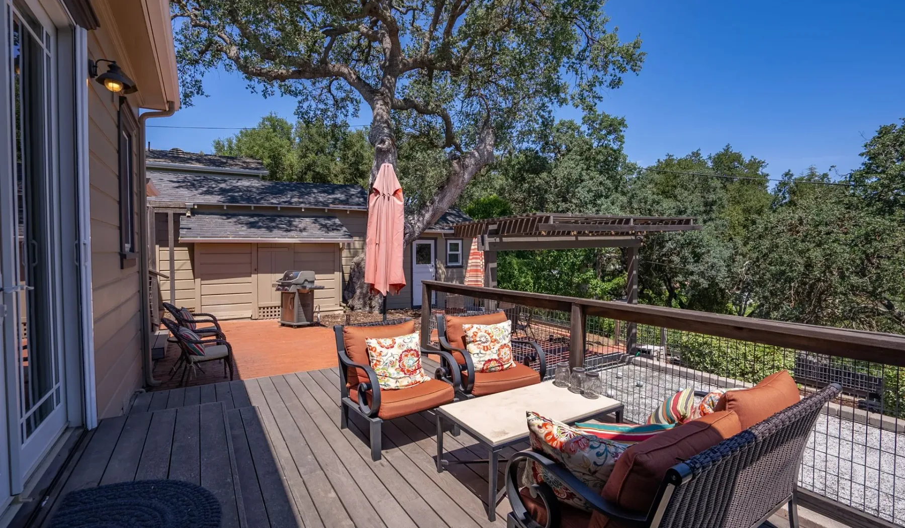 Una terraza de madera con asientos al aire libre, una mesa y un gran árbol.