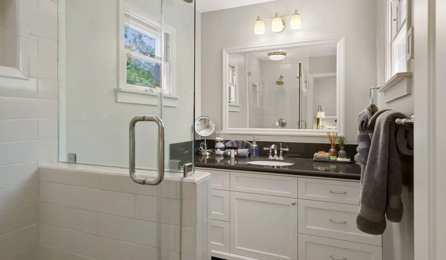 Un baño luminoso con ducha de vidrio, tocador blanco y un espejo grande.