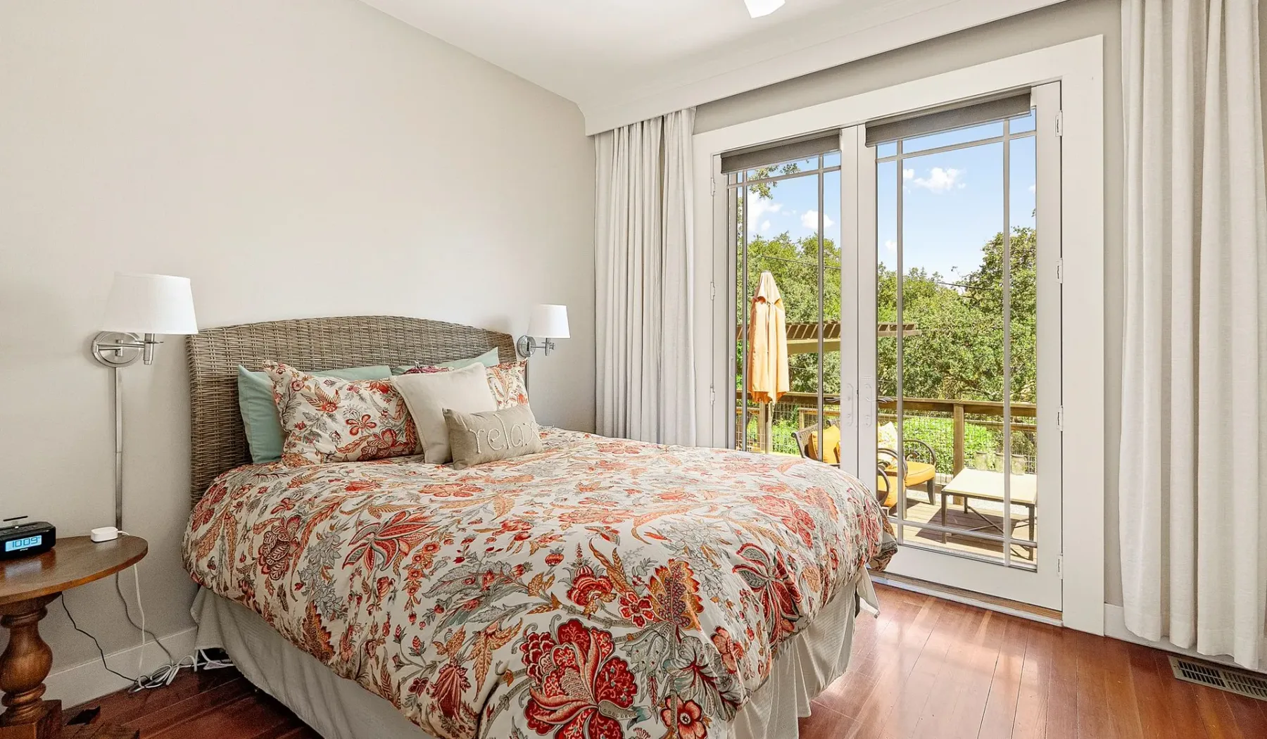Un dormitorio con una colcha floral junto a puertas de vidrio que dan a un balcón.