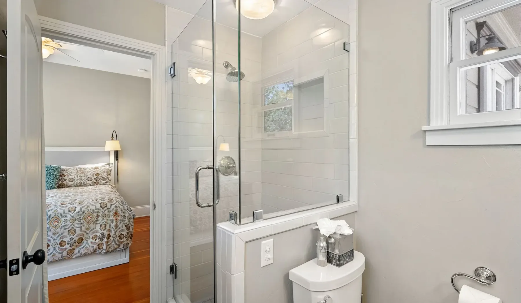 Un baño con ducha de vidrio y un inodoro junto a un dormitorio.