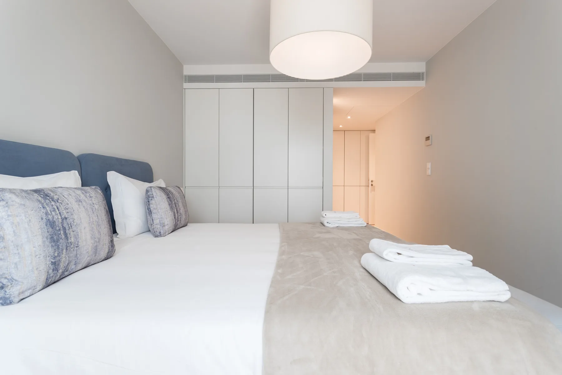 A bright bedroom with a bed, pillows, and folded towels.