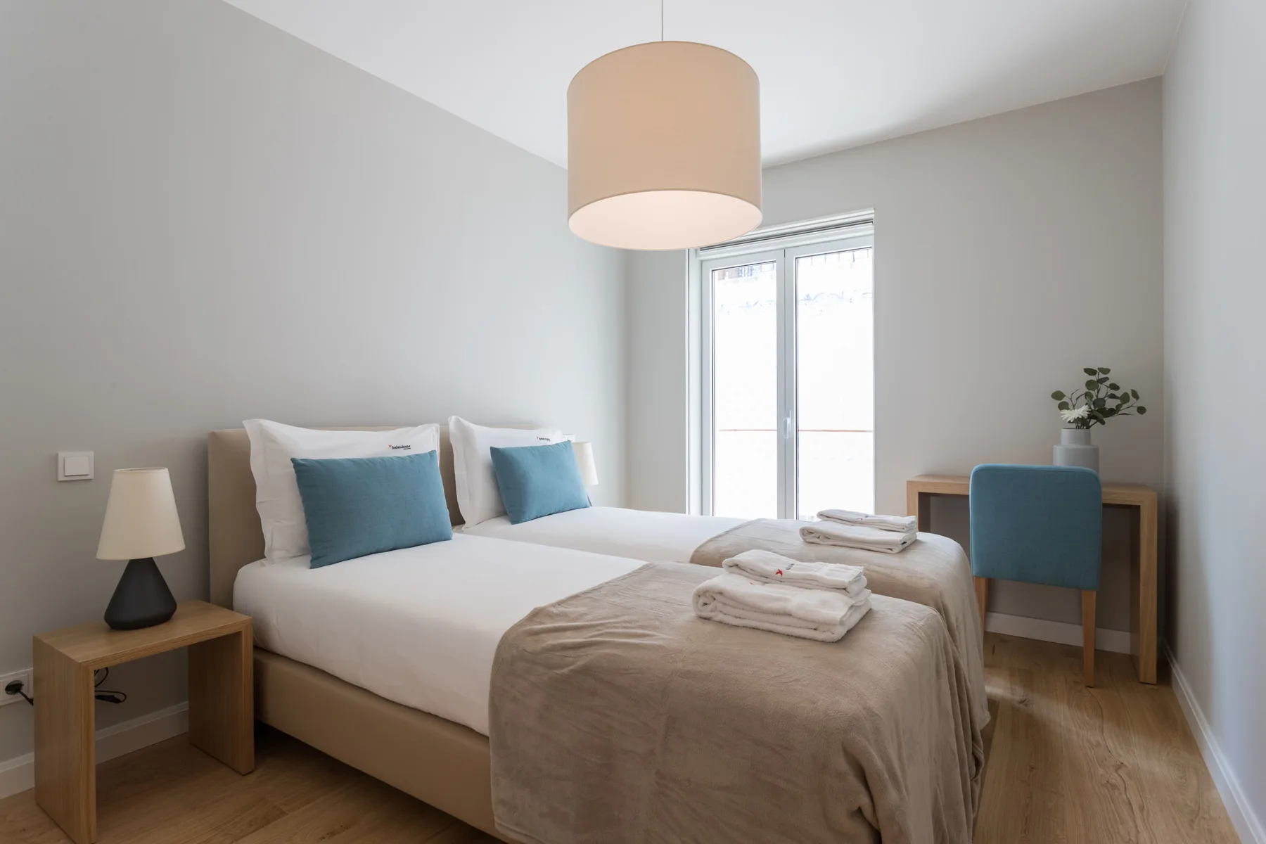 A bedroom with two beds, a desk, and a window.