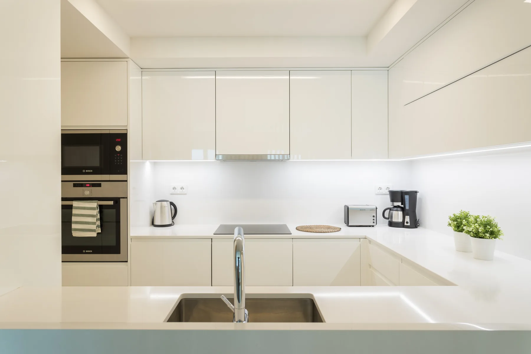 A bright modern kitchen with pale cabinets and a central sink.
