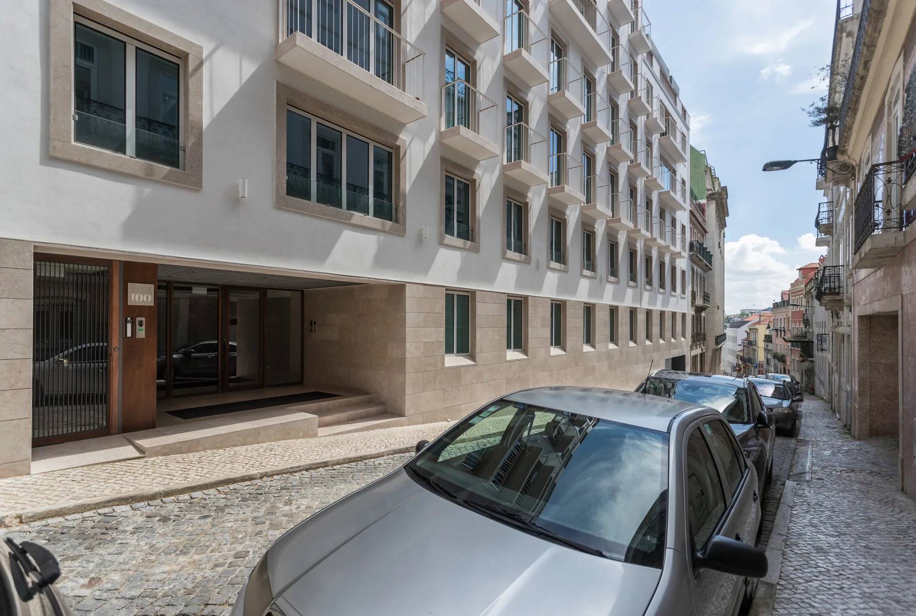 A narrow cobblestone street lined with apartment buildings and parked cars.