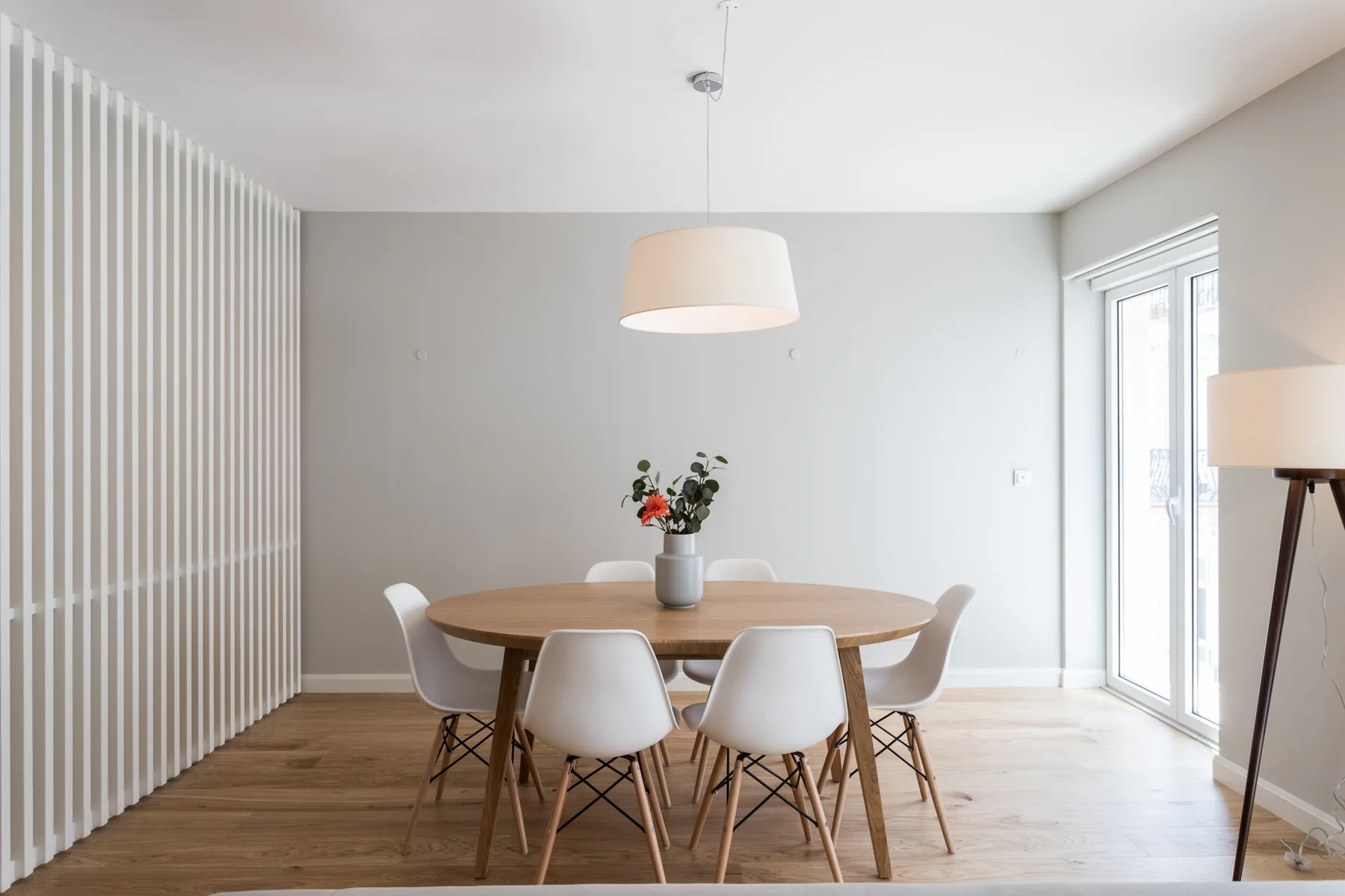 A dining area with a wooden table and chairs beside large windows.