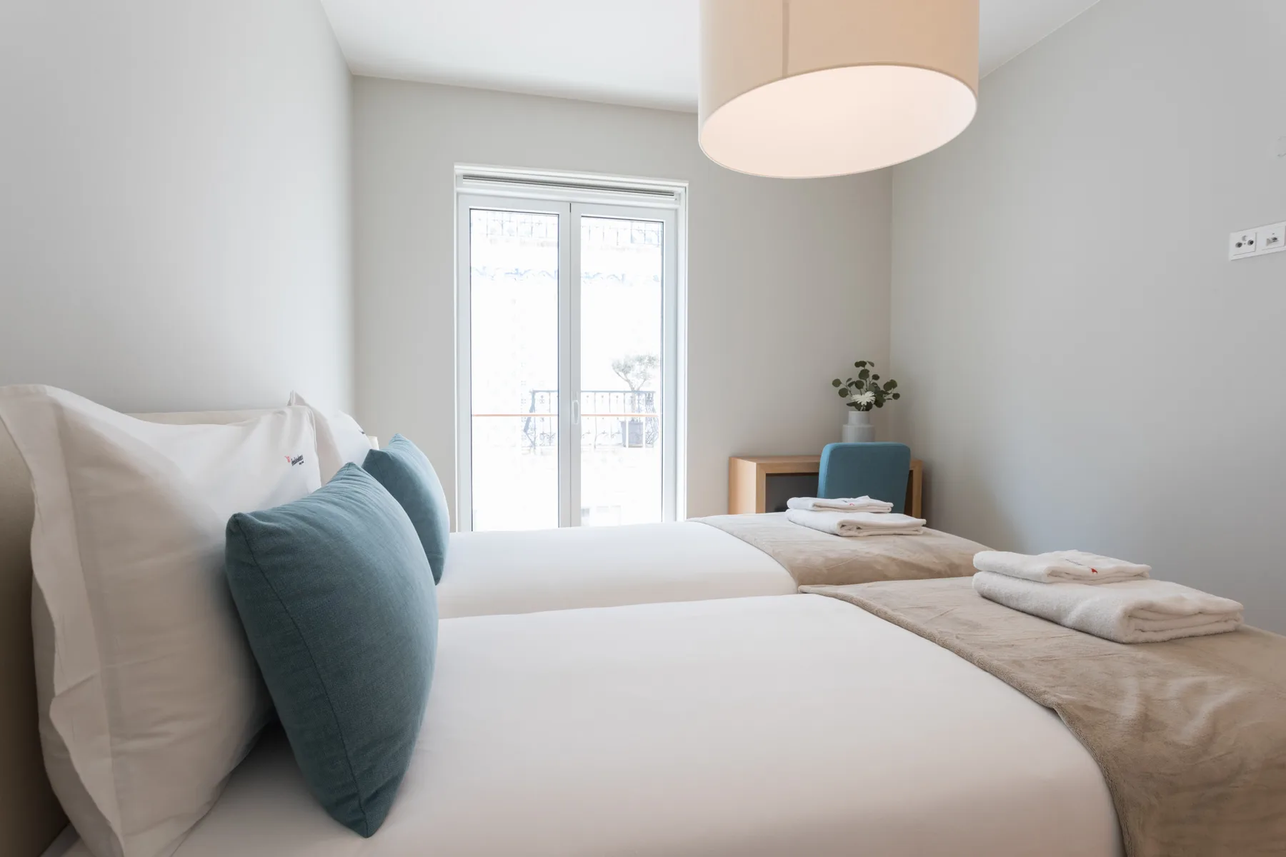 A bright bedroom with two beds and a window.